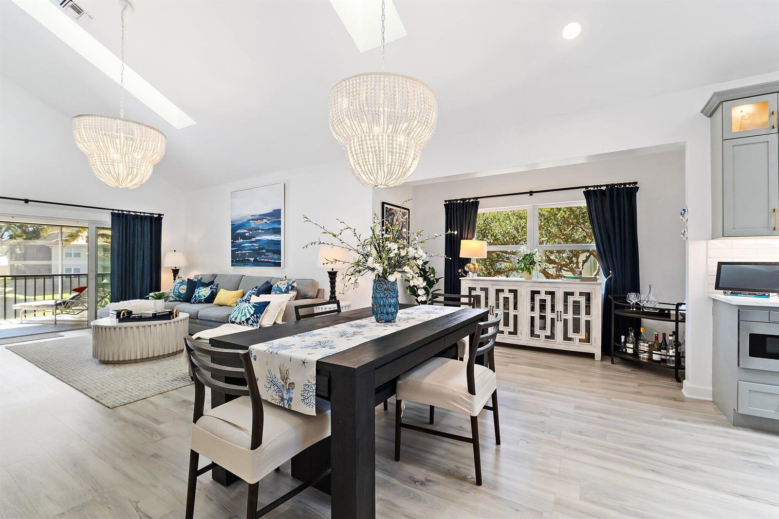 An open-concept living and dining area features vaulted ceilings, bead chandeliers, and light wood flooring — 4161 S Us Highway 1 # E3, Jupiter FL 33477, JUPITER, FL