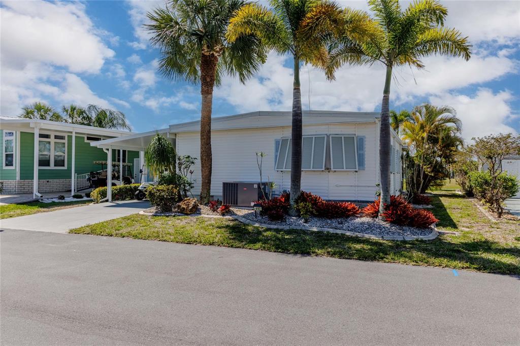 A white manufactured home with a carport and palm trees in a sunny neighborhood — 2100 KINGS HIGHWAY UNIT 497, PORT CHARLOTTE, FL