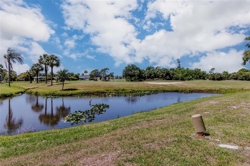 A pond sits in the foreground of a grassy golf course under a cloudy sky — 2100 KINGS HIGHWAY UNIT 497, PORT CHARLOTTE, FL