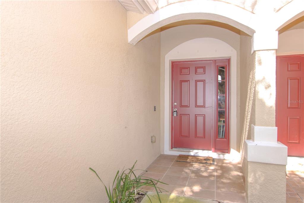 A red front door with a sidelight is set within a covered entryway with tile flooring — 2722 CONCH HOLLOW DRIVE, BRANDON, FL