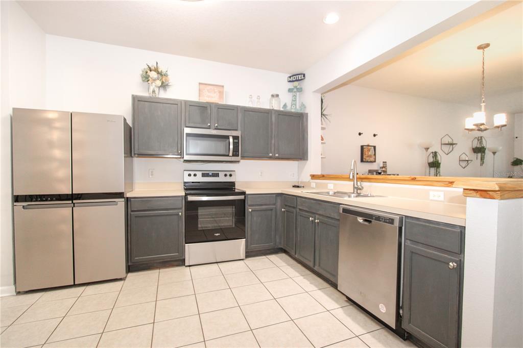 A kitchen features gray cabinets, stainless steel appliances, and light-colored tile flooring — 2722 CONCH HOLLOW DRIVE, BRANDON, FL