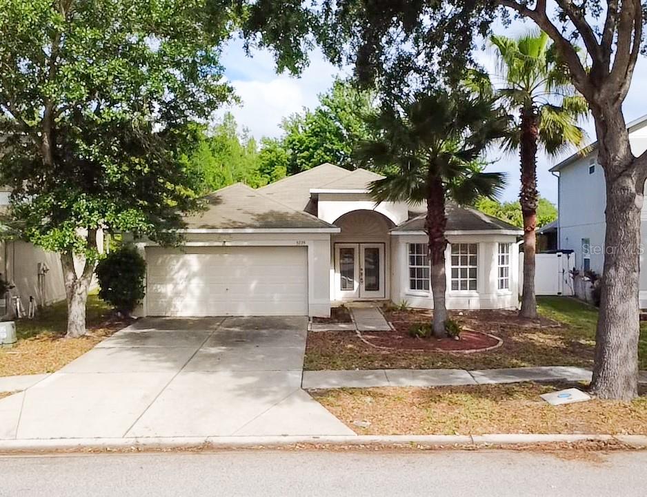 A single-story suburban house with a two-car garage, arched entryway, and two palm trees — 3229 DUNSTABLE DRIVE, LAND O LAKES, FL