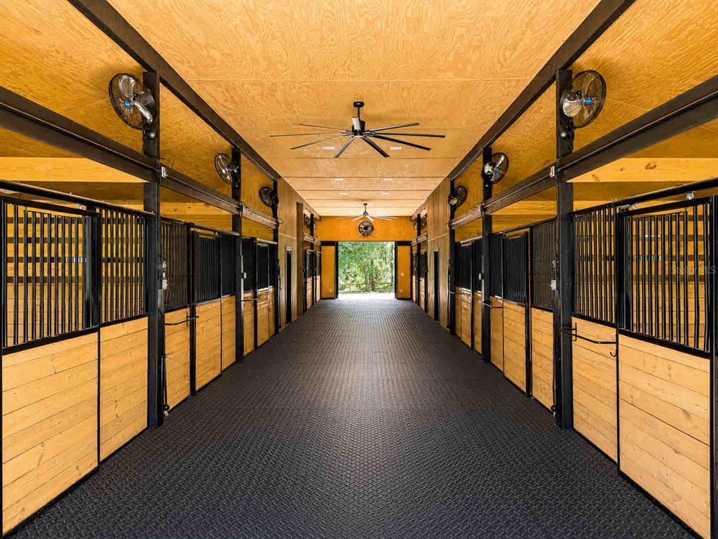 A horse stable aisle features black metal stalls, wood-paneled walls, and a rubber-matted floor — 196 NW 100TH AVENUE, OCALA, FL
