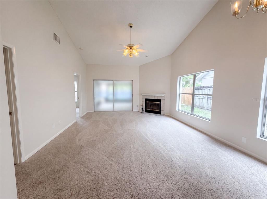 A spacious living room features vaulted ceilings, beige carpeting, a fireplace, and sliding glass doors — 8613 COTTONWAY LANE, TAMPA, FL