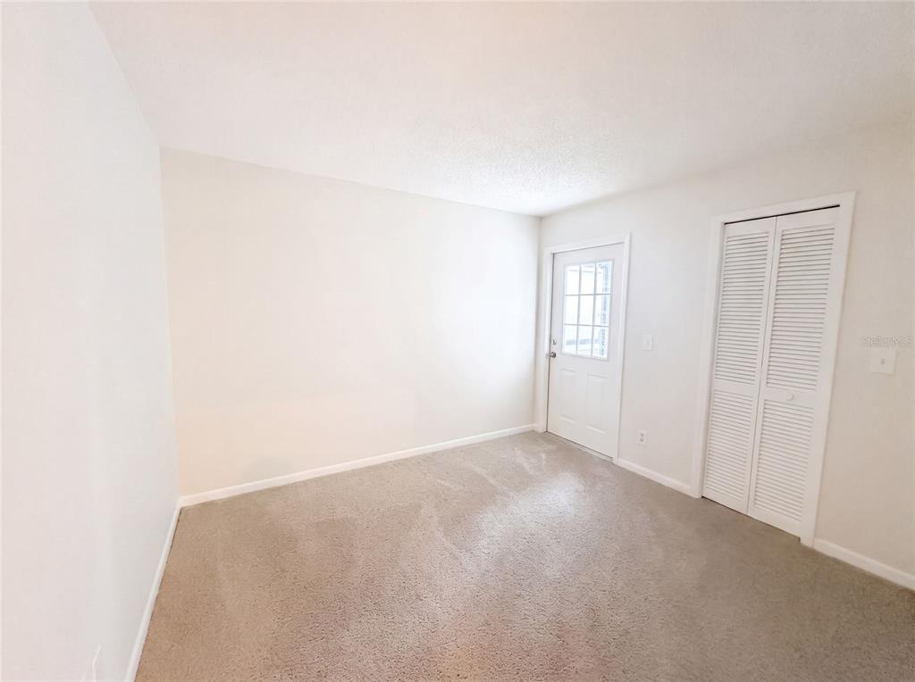 An empty room with beige carpet, white walls, a white door, and a louvered closet — 8613 COTTONWAY LANE, TAMPA, FL