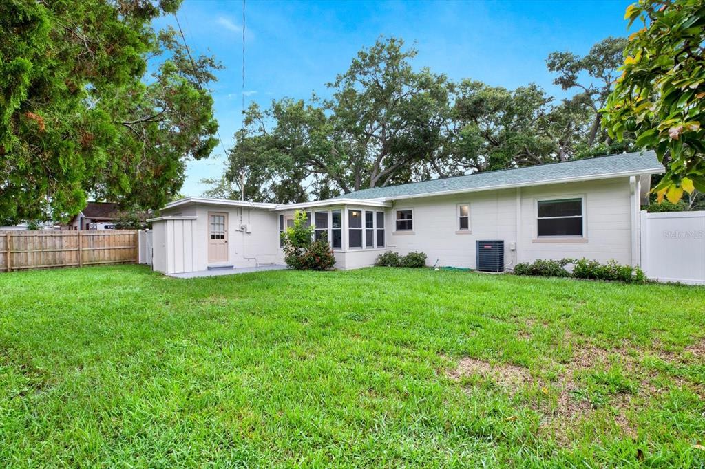 The exterior of a single-story house features a grassy backyard, a sunroom, and mature trees — 8567 RIDGE ROAD, SEMINOLE, FL