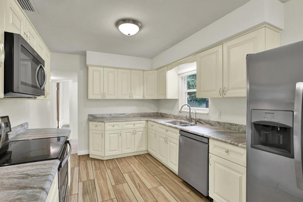 A kitchen features cream-colored cabinets, stone-patterned countertops, stainless steel appliances, and wood-look tile flooring — 8567 RIDGE ROAD, SEMINOLE, FL