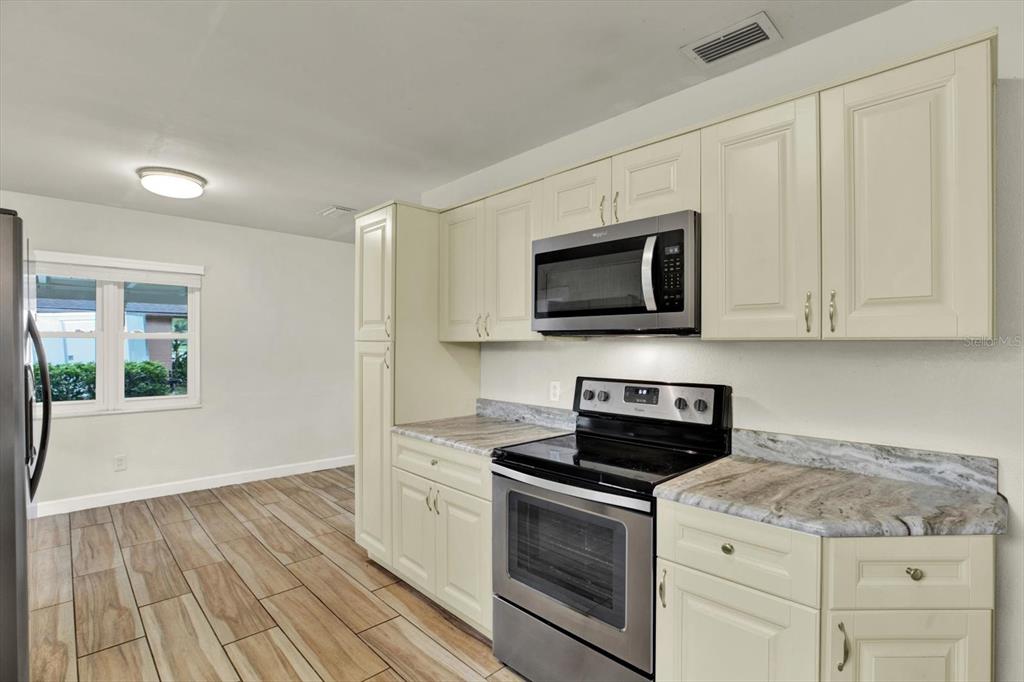 A kitchen with cream-colored cabinets, stainless steel appliances, and wood-look tile flooring — 8567 RIDGE ROAD, SEMINOLE, FL