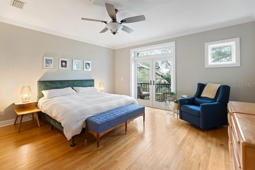 A bedroom with hardwood floors, a green upholstered bed, a blue armchair, and French doors — 514 S GLEN AVENUE, TAMPA, FL