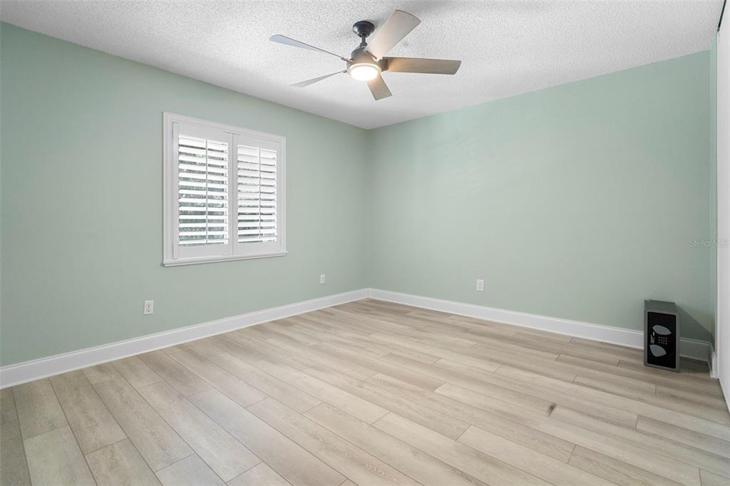 An empty bedroom features light green walls, wood-look flooring, a ceiling fan, and plantation shutters — 5 ESCONDIDO CIRCLE UNIT 46, ALTAMONTE SPRINGS, FL