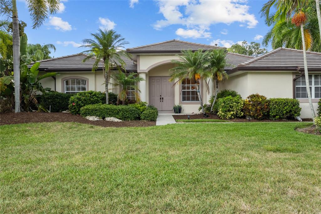 A single-story house with a tiled roof, beige stucco exterior, and a landscaped front yard — 8315 DEERBROOK CIRCLE, SARASOTA, FL