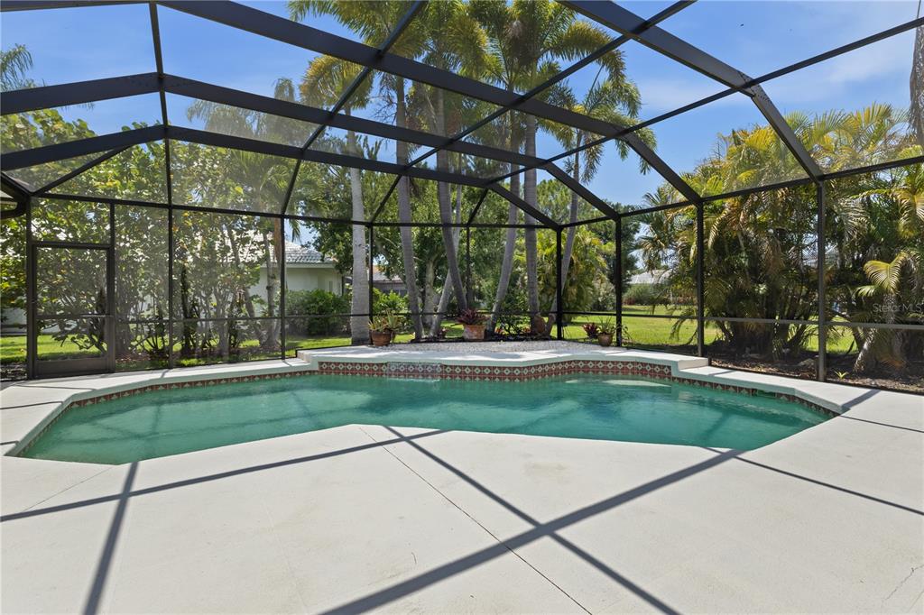 A screened-in swimming pool with a tiled edge and a concrete deck surrounded by palms — 8315 DEERBROOK CIRCLE, SARASOTA, FL