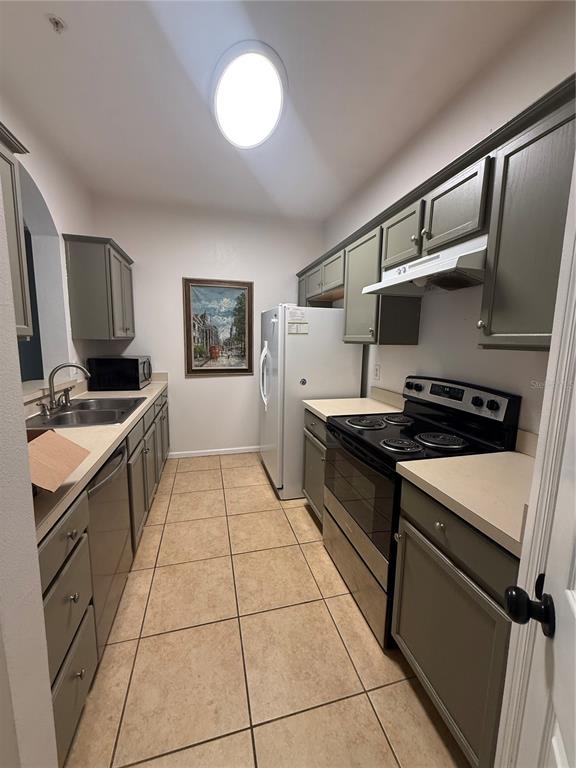 A galley kitchen features olive green cabinets, tan countertops, tile flooring, and stainless steel appliances — 6214 STEVENSON DRIVE UNIT 305, ORLANDO, FL