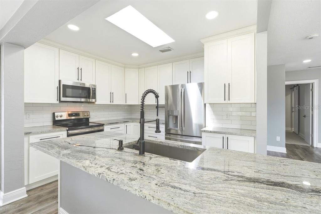 A modern kitchen features white cabinets, granite countertops, stainless steel appliances, and a central island — 105 MCDONALD STREET, SOUTH DAYTONA, FL