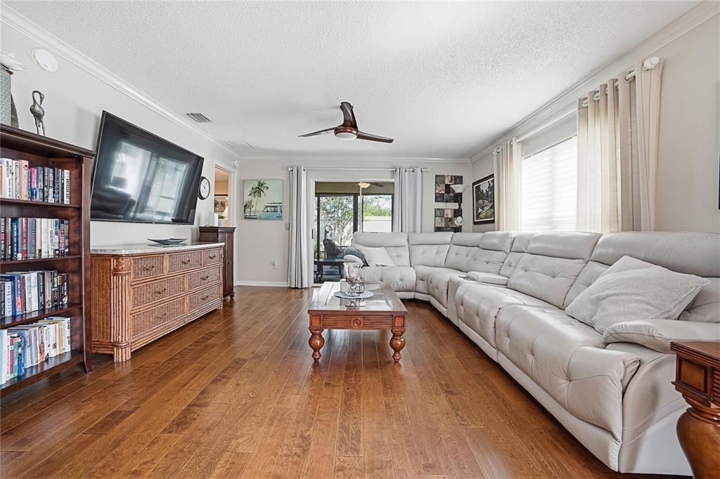 A living room features light gray walls, hardwood floors, a large sectional, and a bookshelf — 1472 ALEXA PLACE, THE VILLAGES, FL