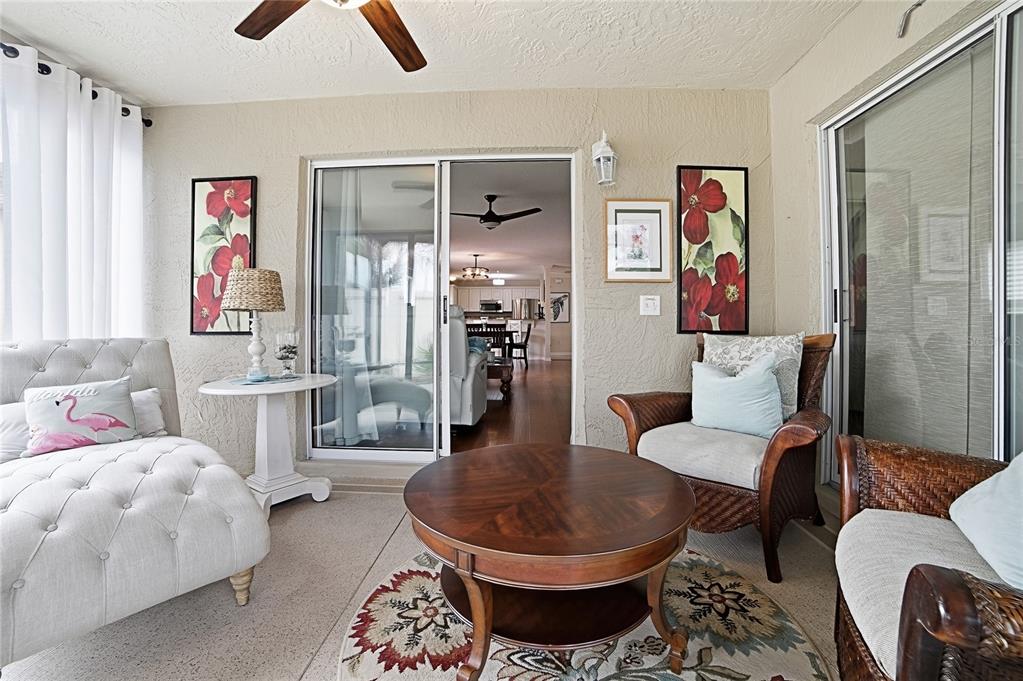 A sunroom features a tufted daybed, wicker chairs, a round coffee table, and sliding glass doors — 1472 ALEXA PLACE, THE VILLAGES, FL