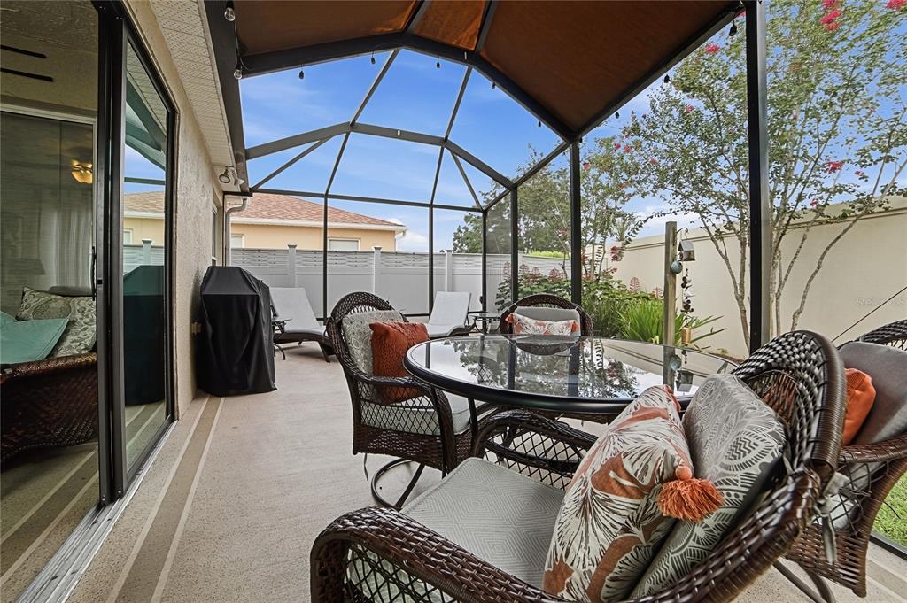 A screened-in patio features wicker furniture, a glass-topped table, and a grill under a roof — 1472 ALEXA PLACE, THE VILLAGES, FL