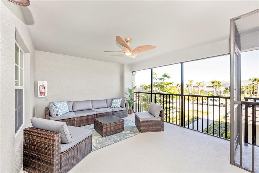 A screened-in balcony features wicker patio furniture, a ceiling fan, and a view of trees — 17500 OPAL SAND DRIVE UNIT 204, VENICE, FL