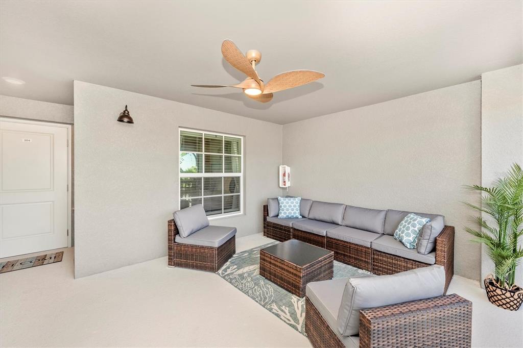 A covered patio features wicker furniture, a ceiling fan, and a light-colored concrete floor — 17500 OPAL SAND DRIVE UNIT 204, VENICE, FL
