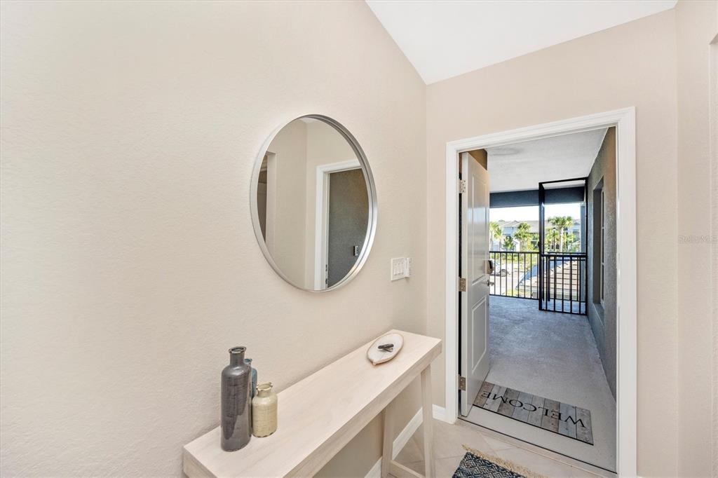 An entryway features a console table, a round mirror, and a door opening to a balcony — 17500 OPAL SAND DRIVE UNIT 204, VENICE, FL