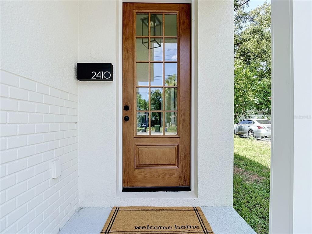A wooden front door with glass panes sits between white walls with a welcome mat — 2410 E 20TH AVENUE, TAMPA, FL