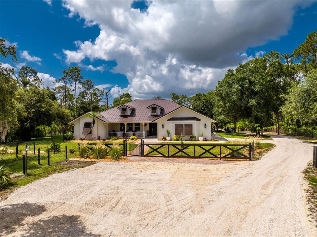 A single-story house with a metal roof sits behind a black wooden gate and driveway — 8007 ESTATES DRIVE, NORTH PORT, FL