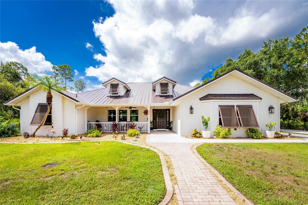 A white single-story house with a metal roof, front porch, and brick walkway — 8007 ESTATES DRIVE, NORTH PORT, FL