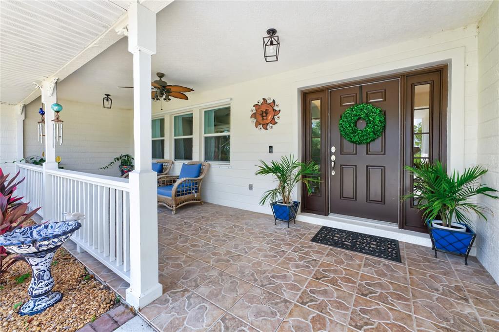 A covered front porch features tiled flooring, wicker chairs, potted plants, and a brown front door — 8007 ESTATES DRIVE, NORTH PORT, FL