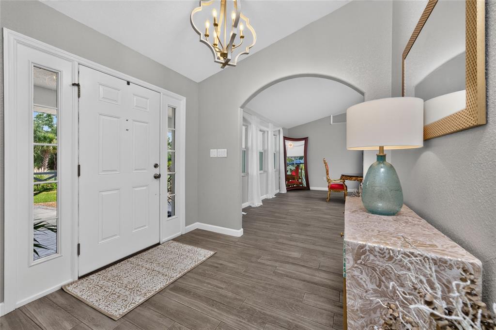 An entryway features a white door with sidelights, wood-look flooring, and an arched doorway — 8007 ESTATES DRIVE, NORTH PORT, FL