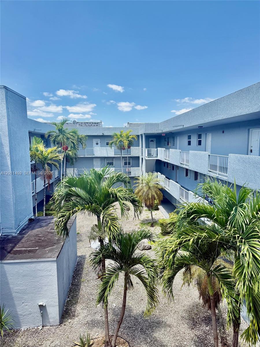An outdoor courtyard with palm trees is surrounded by a multi-story blue apartment building — 1755 W 60th St # D312, Hialeah FL 33012, HIALEAH, FL