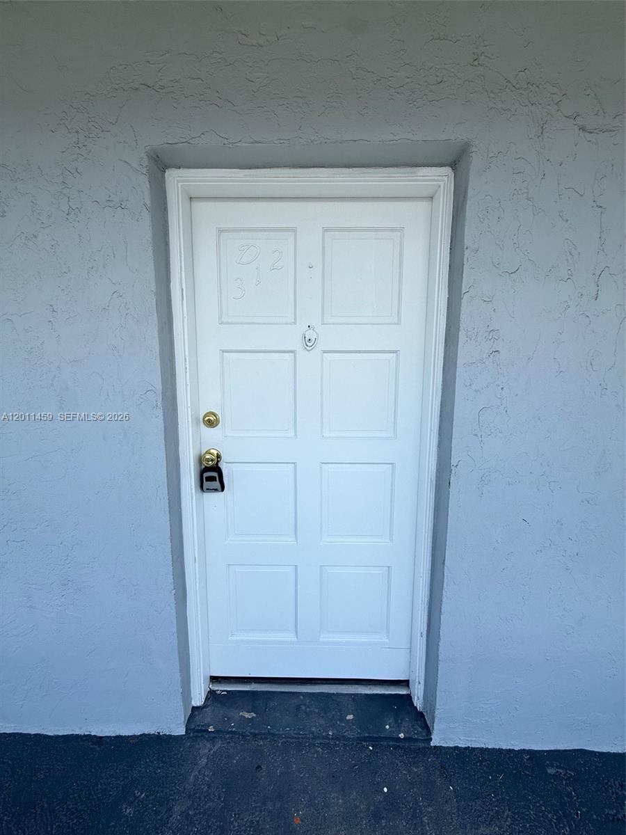 A white six-panel exterior door with a lockbox is set into a light gray wall — 1755 W 60th St # D312, Hialeah FL 33012, HIALEAH, FL