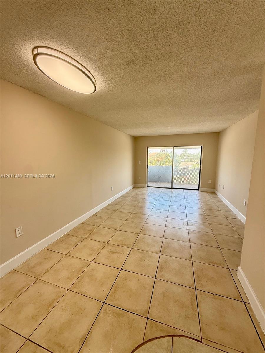 An empty room features beige walls, a tiled floor, and sliding glass doors to a balcony — 1755 W 60th St # D312, Hialeah FL 33012, HIALEAH, FL