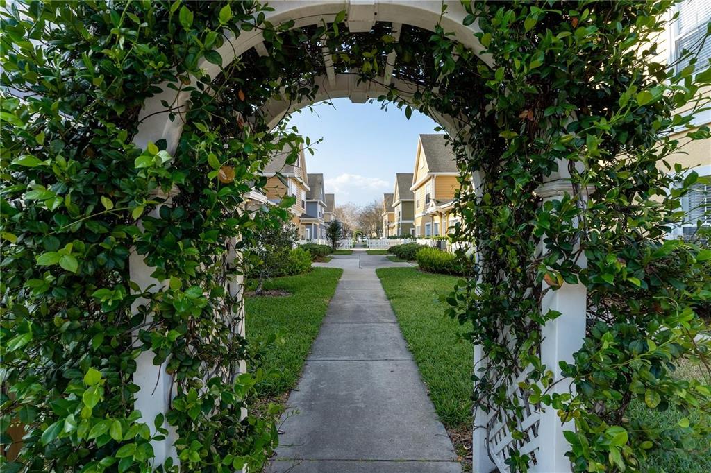 A white wooden trellis covered in vines frames a sidewalk leading between suburban houses — 2622 LODI CIRCLE UNIT 103, KISSIMMEE, FL