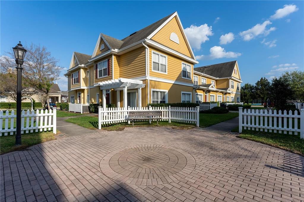 A yellow two-story building with a white picket fence and a circular brick patio — 2622 LODI CIRCLE UNIT 103, KISSIMMEE, FL