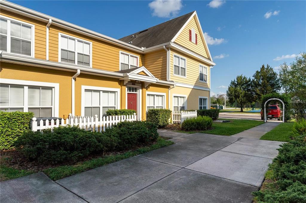 A yellow two-story townhouse features a red front door, white trim, and a concrete driveway — 2622 LODI CIRCLE UNIT 103, KISSIMMEE, FL