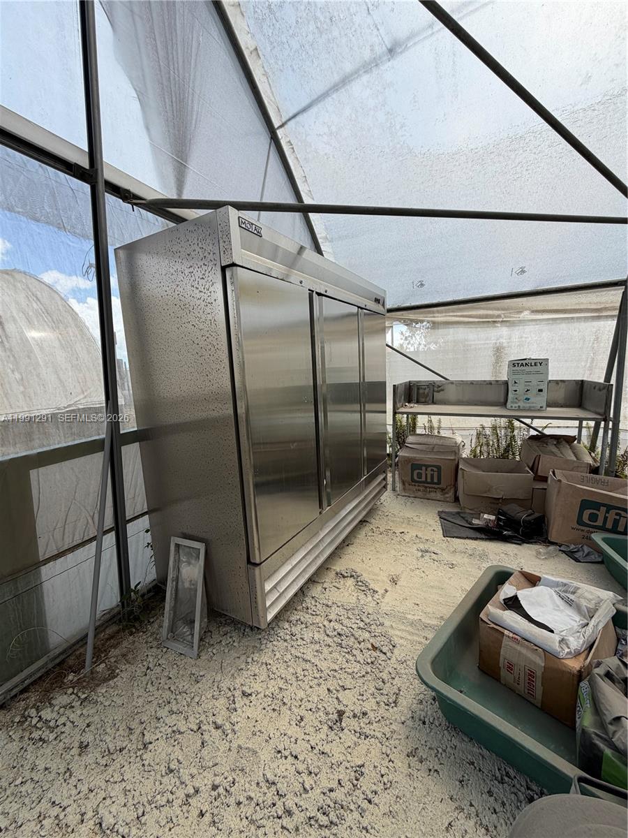 A large stainless steel commercial refrigerator sits inside a greenhouse structure with gravel flooring — SW 169 Ave, Miami FL 33187, MIAMI, FL