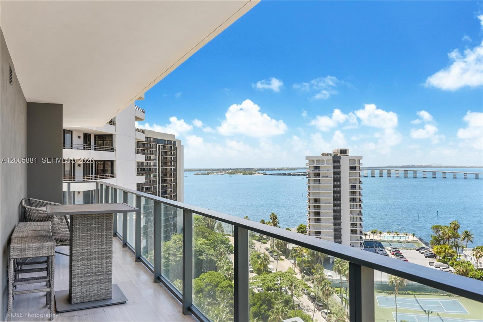 A balcony with outdoor furniture overlooks a bay, a bridge, and nearby residential buildings — 1451 Brickell Ave # 1203, Miami FL 33131, MIAMI, FL
