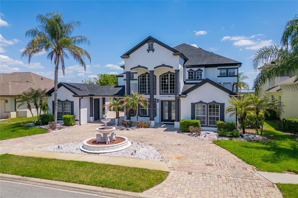 A two-story white house with dark trim, a stone driveway, and a front yard fountain — 1407 WATER LILLY LANE, KISSIMMEE, FL