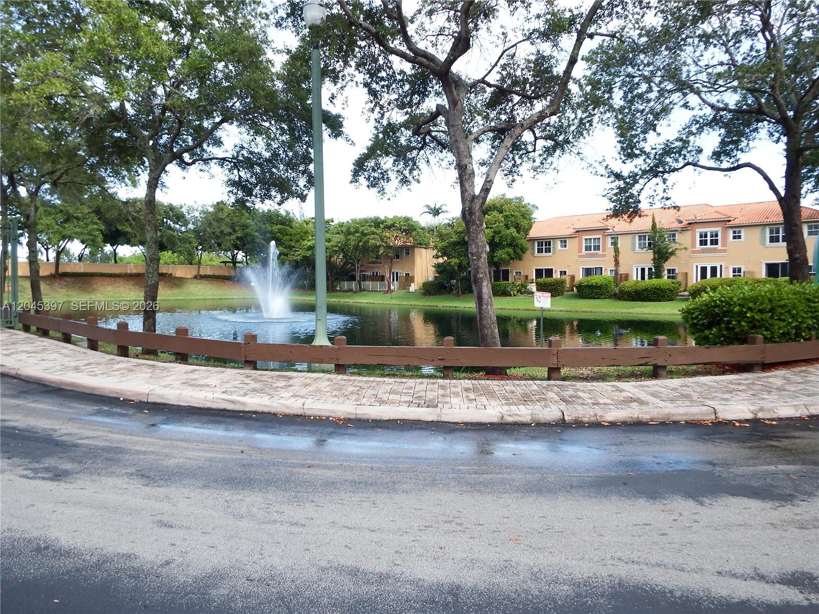 A fountain sits in a pond behind a wooden fence near residential buildings — 4943 Leeward Ln # 3204, Dania Beach FL 33312, DANIA BEACH, FL