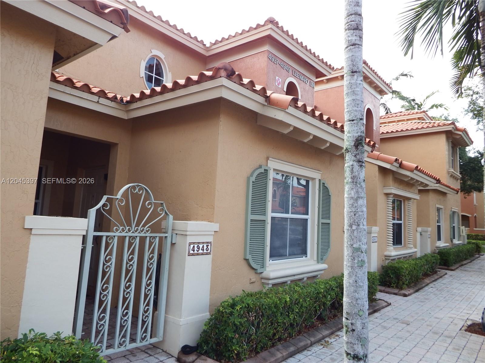 A tan stucco townhouse exterior features a decorative metal gate, green shutters, and tile roofing — 4943 Leeward Ln # 3204, Dania Beach FL 33312, DANIA BEACH, FL