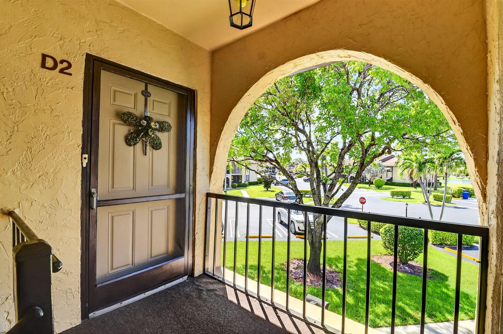 An apartment entrance with a screen door, a dragonfly wreath, and an arched balcony view — 207 Pine Hov Circle # D2, FL 33463, FL