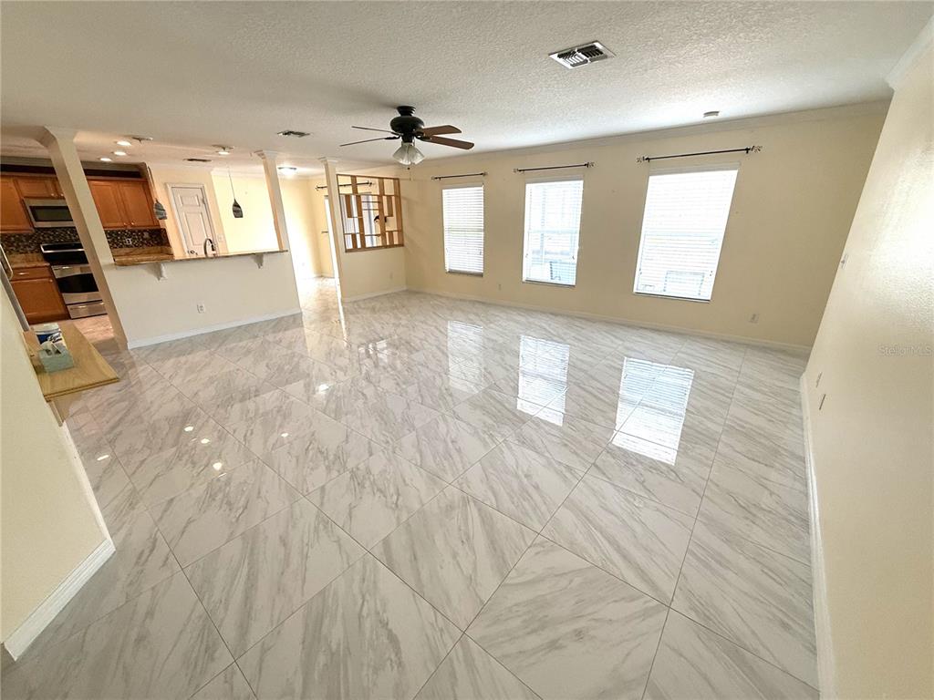 A spacious living room features light-colored marble-look tile flooring and three large windows — 344 SKY VALLEY STREET, CLERMONT, FL