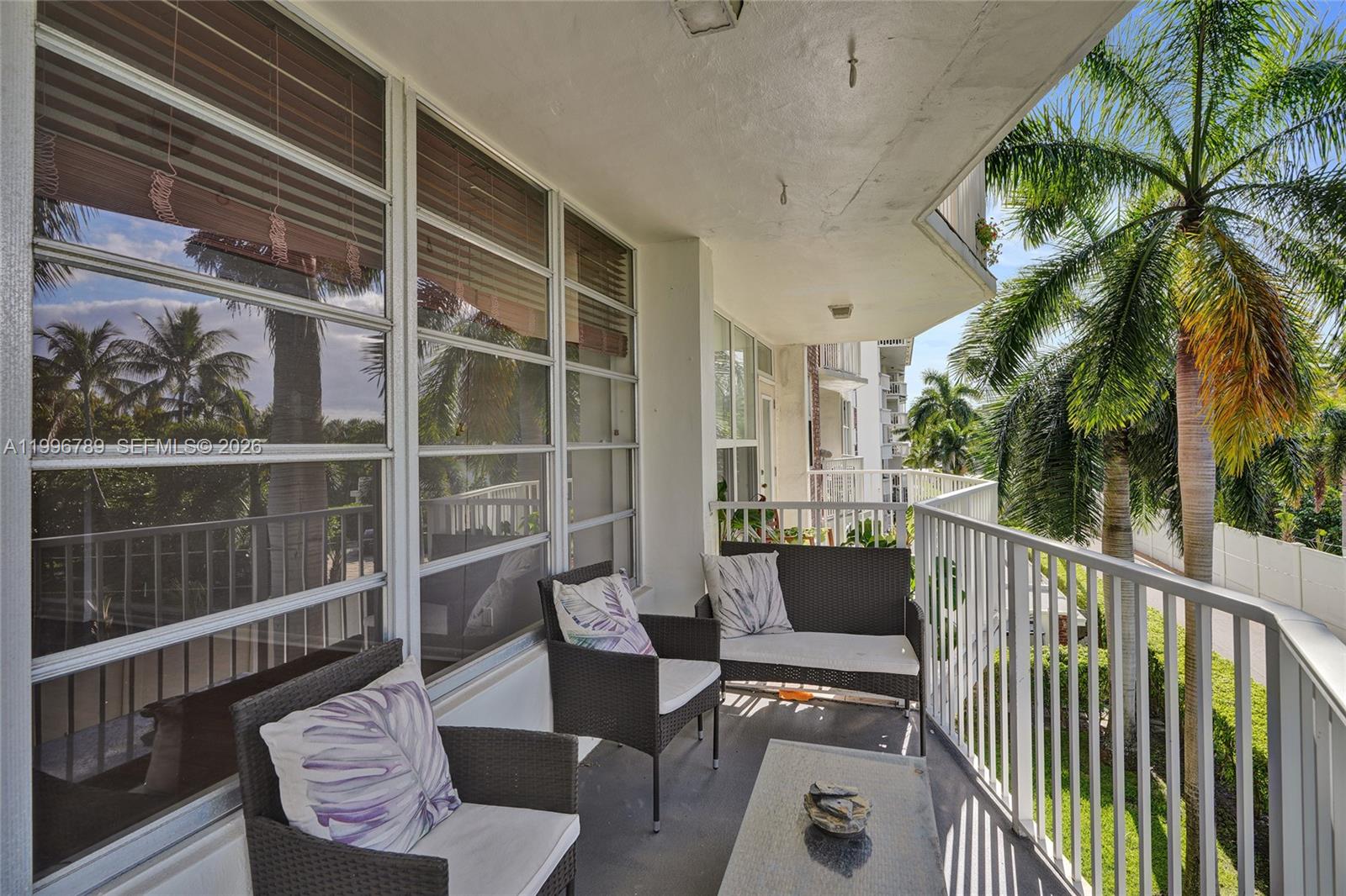 A balcony features wicker furniture, a glass-topped table, and views of palm trees — 3181 S Ocean Dr, Hallandale Beach FL 33009, HALLANDALE BEACH, FL