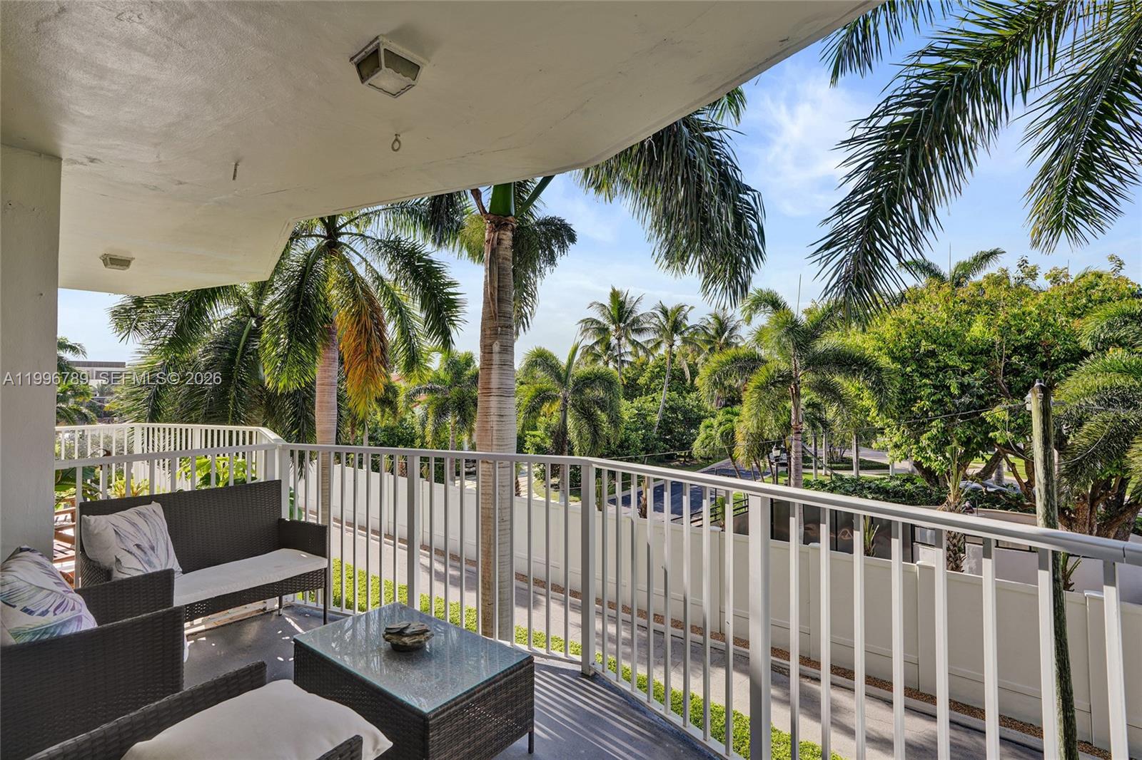A balcony with wicker furniture overlooks a lush tropical landscape with palm trees — 3181 S Ocean Dr, Hallandale Beach FL 33009, HALLANDALE BEACH, FL