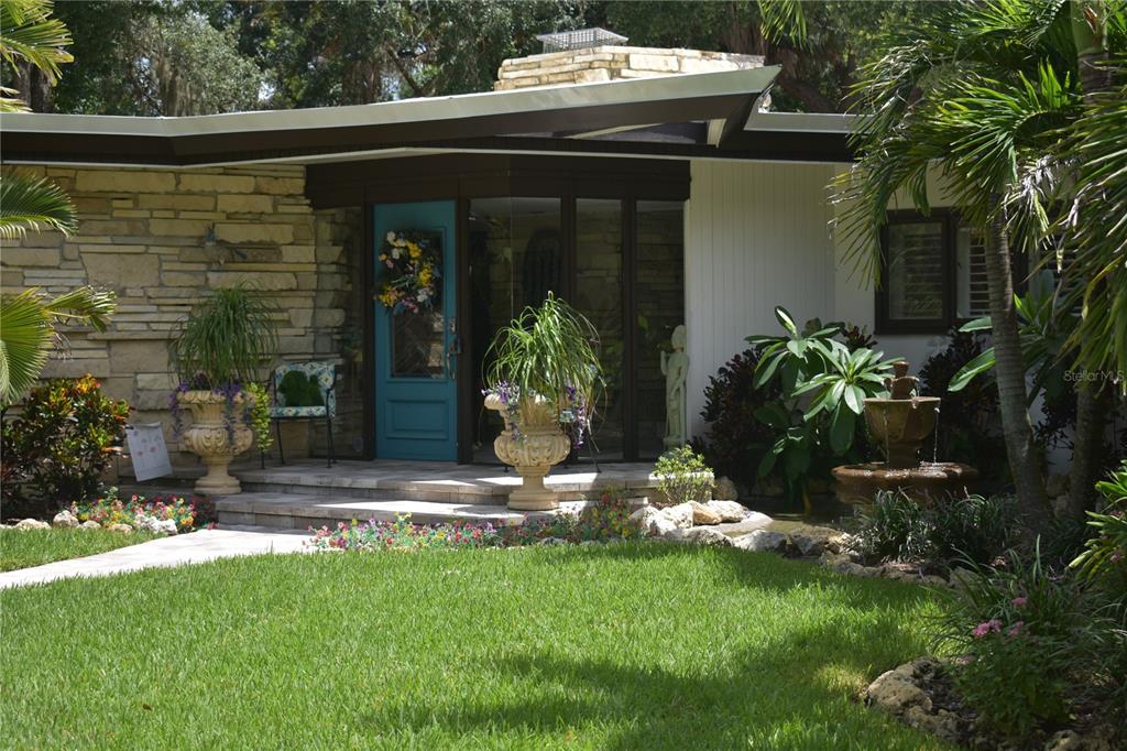 A mid-century modern home exterior features a stone facade, a teal door, and a fountain — 1653 SUNNYBROOK LANE, CLEARWATER, FL