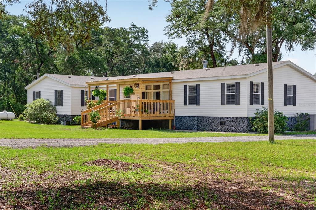 A single-story manufactured home with light siding, a wooden front deck, and stone-patterned skirting — 15680 SE 171ST LANE, WEIRSDALE, FL
