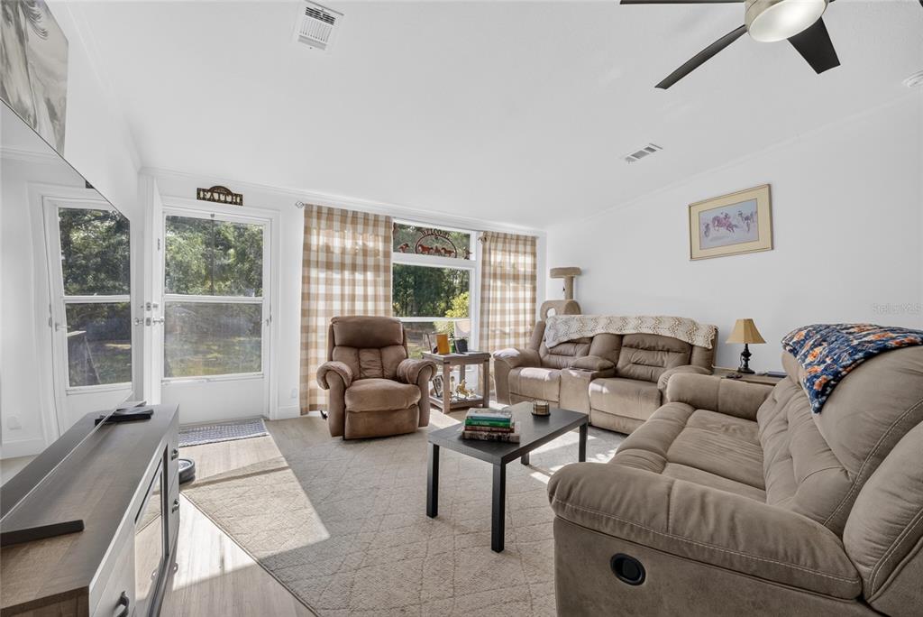A living room features light wood flooring, tan furniture, a coffee table, and large windows — 15680 SE 171ST LANE, WEIRSDALE, FL