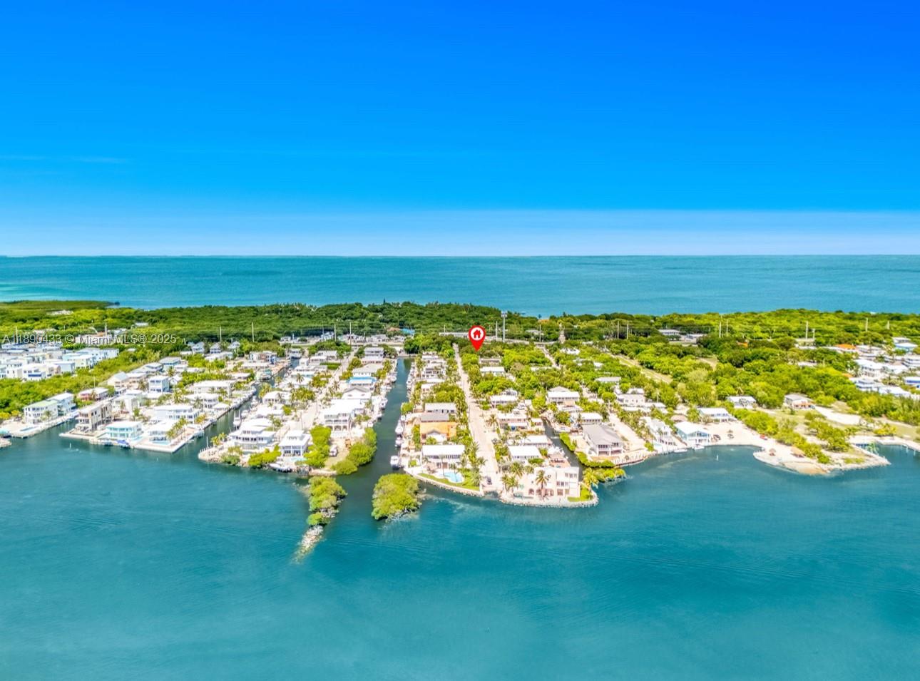 An aerial view shows a coastal neighborhood with houses along a canal and the ocean — 933 Lobster Ln, Key Largo FL 33037, KEY LARGO, FL