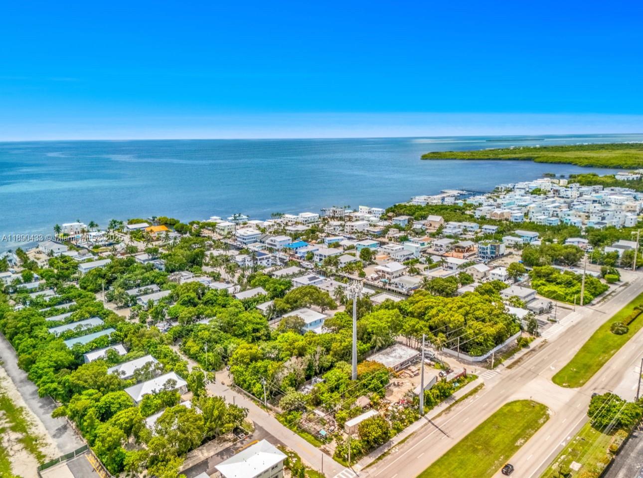 An aerial view shows a coastal neighborhood with many houses, lush trees, and a road — 933 Lobster Ln, Key Largo FL 33037, KEY LARGO, FL