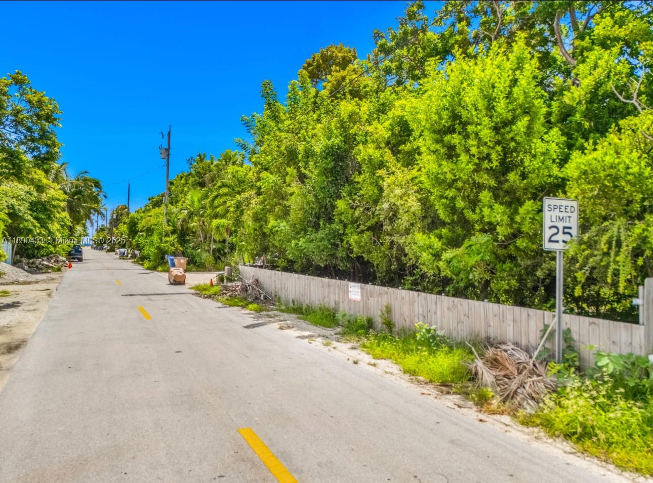 A paved road with a speed limit sign runs alongside a wooden fence and trees — 933 Lobster Ln, Key Largo FL 33037, KEY LARGO, FL